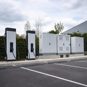 Armoires de batteries stationnaires à côté de bornes de recharge sur un parking, en France.