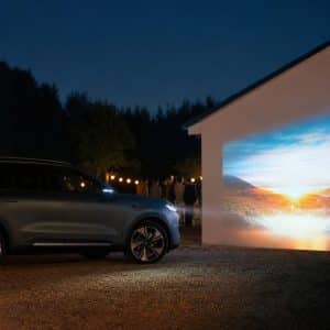 Un SUV électrique projetant une image colorée sur un mur lors d’une soirée en plein air, illustration de la fonction projecteur.