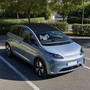 Une voiture électrique garée au soleil avec un toit sombre évoquant des cellules solaires, sur un parking extérieur