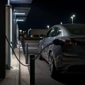 Station de recharge rapide sur autoroute avec une voiture électrique branchée, ambiance nocturne réaliste