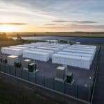 Conteneurs de batteries près d’une installation solaire avec lignes électriques en arrière-plan