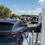 Voiture électrique en recharge sur une aire d’autoroute estivale avec circulation dense en arrière-plan