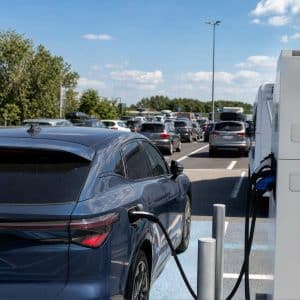 Voiture électrique en recharge sur une aire d’autoroute estivale avec circulation dense en arrière-plan