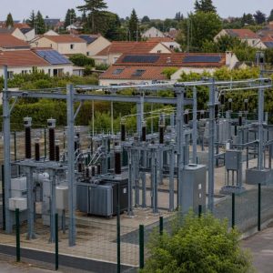 Technicien observant un poste électrique près de maisons équipées de panneaux solaires