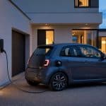Voiture électrique blanche branchée devant une maison française au début de la soirée