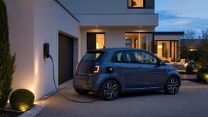 Voiture électrique blanche branchée devant une maison française au début de la soirée