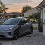 Voiture électrique en recharge à domicile avec une station-service visible au loin