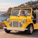 Moke électrique Mk2 jaune photographiée sur une route côtière, vue de trois-quarts avant