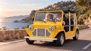 Moke électrique Mk2 jaune photographiée sur une route côtière, vue de trois-quarts avant