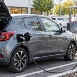 Voiture électrique compacte branchée sur une borne standard dans un parking de supermarché, illustration sans marque